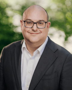 Headshot of a white man with glasses, white shirt, and blazer.