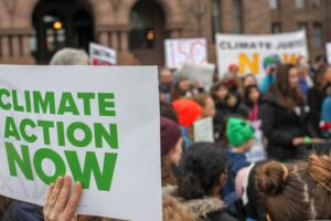 A photograph of a climate protest focused on a sign that reads “Climate Action Now.”