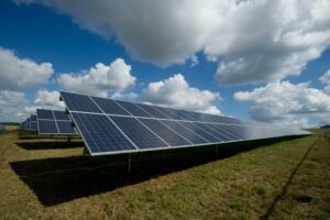 Field of solar panels with sky and clouds in the background.